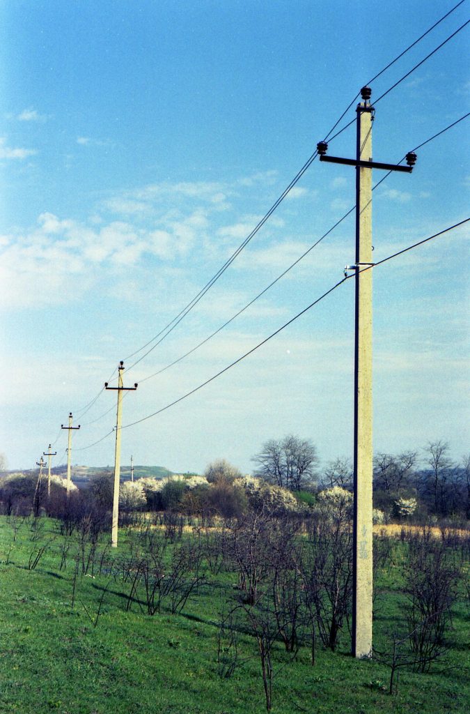 A scenic view of power lines traversing a green meadow under a clear blue sky.